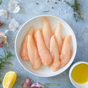 Fresh, raw chicken tenderloins in a bowl surrounded by ingredients.
