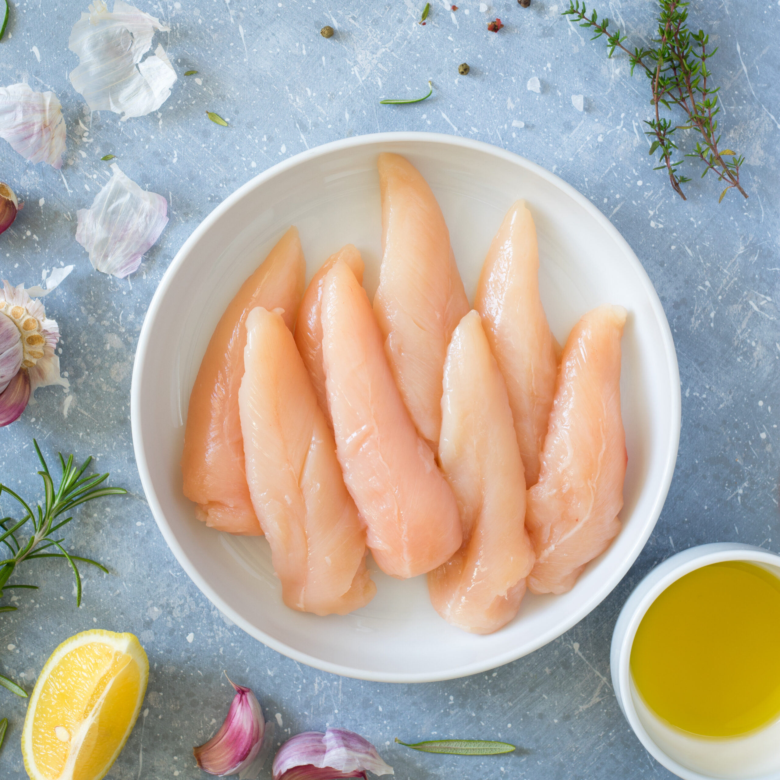 Fresh, raw chicken tenderloins in a bowl surrounded by ingredients.